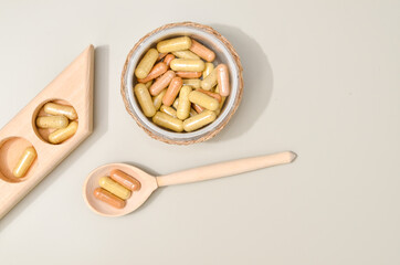 Herb in capsules in wooden bowl on pastel beige background. Beauty products for face and body skin care