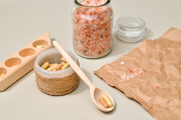 Herb in capsules in wooden bowl on pastel beige background. Beauty products for face and body skin care