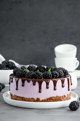Blackberry cream mousse cake (no baked cheesecake) with chocolate glaze on a white plate on a dark...