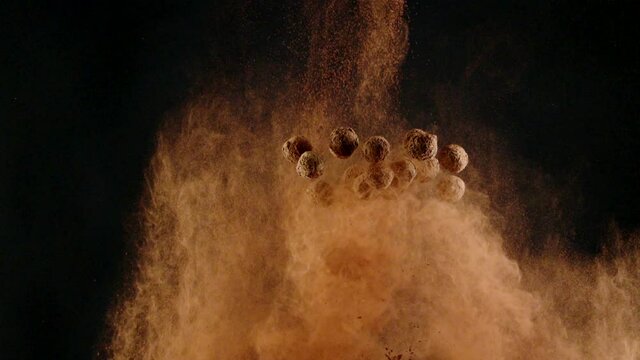 Luxury Handmade Truffle sweets fly into falling cocoa powder cloud slow motion isolated on black backdrop. Sweet taste explosion concept. Advertising for premium handcrafted confectionary shop