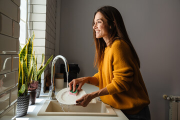 Beautiful middle-aged woman smiling while washing dishes at home