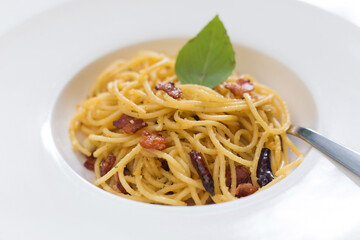 Stir fried spaghetti with dried chilli and crispy bacon  in a white dish.