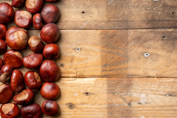 A photo of chestnuts, conkers on a rustic wooden background shot from above, flat lay with copy space. Autumn, fall , winter concept