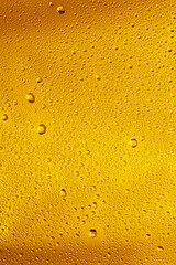 Close up view of cold drops on the glass of beer background. Texture of cooling alcohol drink with macro bubbles on the glass wall. Fizzing or floating up to top of surface. Golden colored.