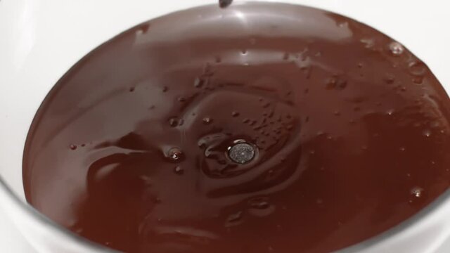 chocolate chips or couverture callets fall in bowl of melted dark chocolate slow mo. Advertising for handcrafted confectionary shop. Culinary Video Blog. Homemade sweeties production