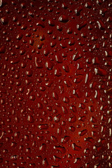 Close up view of cold drops on the glass of beer background. Texture of cooling alcohol drink with macro bubbles on the glass wall. Fizzing or floating up to top of surface. Dark brown colored.