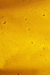 Close up view of cold drops on the glass of beer background. Texture of cooling alcohol drink with macro bubbles on the glass wall. Fizzing or floating up to top of surface. Golden colored.
