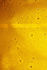 Close up view of cold drops on the glass of beer background. Texture of cooling alcohol drink with macro bubbles on the glass wall. Fizzing or floating up to top of surface. Golden colored.