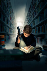 Junge beim Lesen im Dunkeln mit Taschenlampe in der Bibliothek