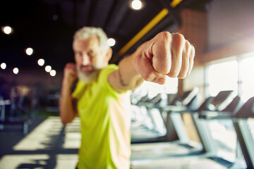 Strength training. Focused mature man in sportswear boxing, while working out at gym, focus on male hand