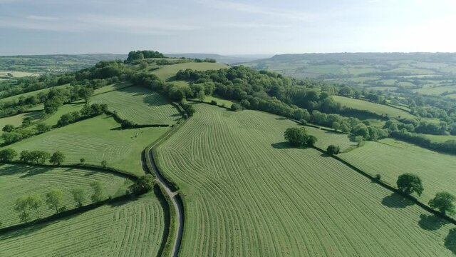 Aerial rising up a solitary hill amongst devon landscape in the english countryside, fields have been cut.