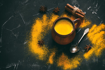 Golden milk with turmeric powder, cinnamon and star anise in a ceramic cup on a black stone...