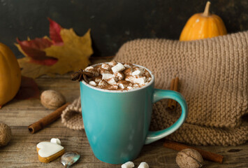 Hot cocoa with marshmallows in a blue ceramic mug with autumn leaves and pumpkins on a wooden table. The concept of hygge, cozy autumn, Thanksgiving, fall. Hot drinks.Autumn Still Life