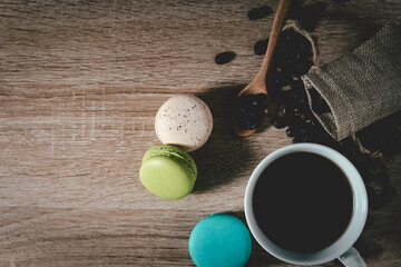 Black Coffee in a cup with coffee beans and macarons on wood table background