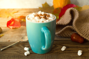 Hot cocoa with marshmallows in a blue ceramic mug with autumn leaves and pumpkins on a wooden table. The concept of hygge, cozy autumn, Thanksgiving, fall. Hot drinks.Autumn Still Life
