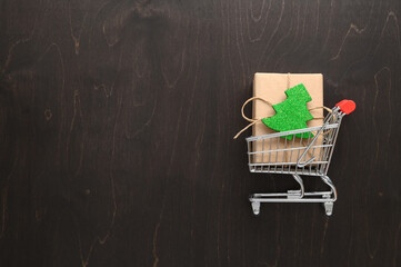 Christmas shopping concept. Top view of shopping cart and gift box on dark brown background. Copy...