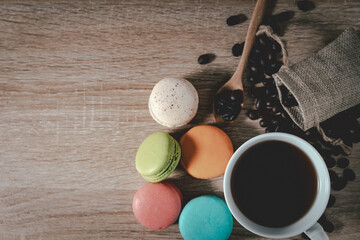 Fototapeta na wymiar Black Coffee in a cup with coffee beans and macarons on wood table background