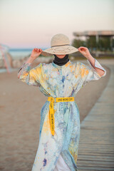 modest girl in a hat near the seashore on the beach, against the blue sky