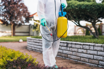 Exterminator in work wear outdoors spraying pesticide with sprayer