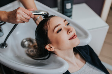 Professional hairdresser washing hair of a beautiful young  woman in hair salon. .