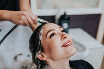 Fototapeta na wymiar Professional hairdresser washing hair of a beautiful young woman in hair salon. .