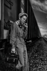 Vintage dirty female worker having her cigarette break leaning against a train wagon