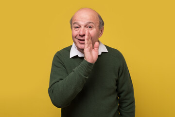 Secret, gossip concept. Senior caucasian man whispering a secret behind his hand. Studio shot.