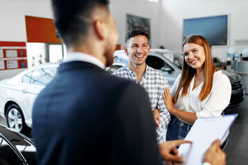 Man car salesman telling about the features of the new car to the couple