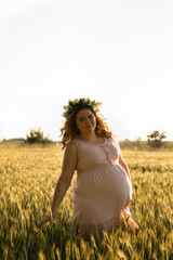Fototapeta na wymiar A pregnant woman in a pink dress walks in nature.