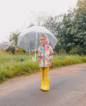 happy girl in bright clothes stands in the rain with a large umbrella in her hands
