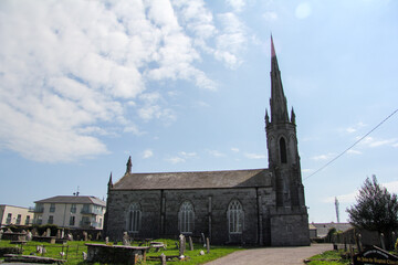 Stone cathedral with a very sharp spike at the top and a cemetery next to it