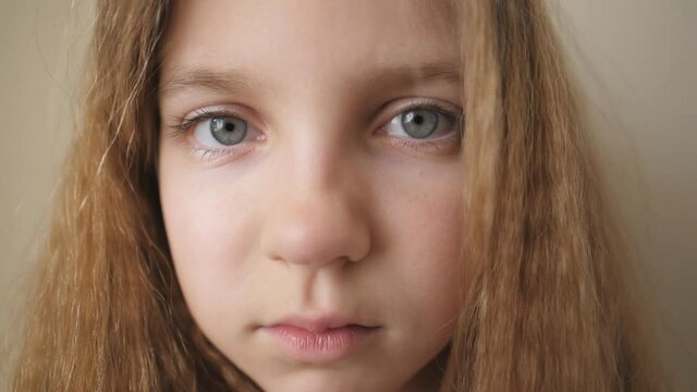 Close up female face of desperate child looking into camera indoor. Disappointed gaze of small upset kid. Portrait of little blonde girl with sorrowful expression inside
