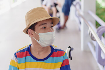 Fototapeta na wymiar Asian special child on wheelchair wearing a protection mask against PM 2.5 air pollution and flu Covid 19 or Coronavirus on public path background, N95 to prevent the spread of the virus disease 2020.