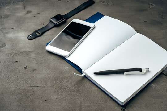 Open notepad, smartphone and smart watch on dark grey background