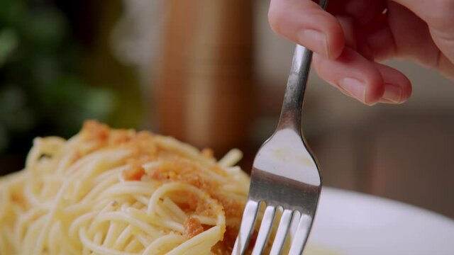 Caucasian fingers with silver fork lifts up delicious tasty traditional Italian cooked pasta dish, Spaghetti alla bottarga, delicacy of salted, aged, cured mullet fish roe, detail close up slow motion