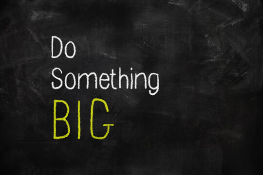 Do something big written with white and yellow chalk on blackboard