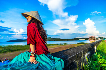 Vietnamese girl sitting on the dike in beautiful sunset with blue sky in Dau Tieng lake, Tay Ninh province, Vietnam.