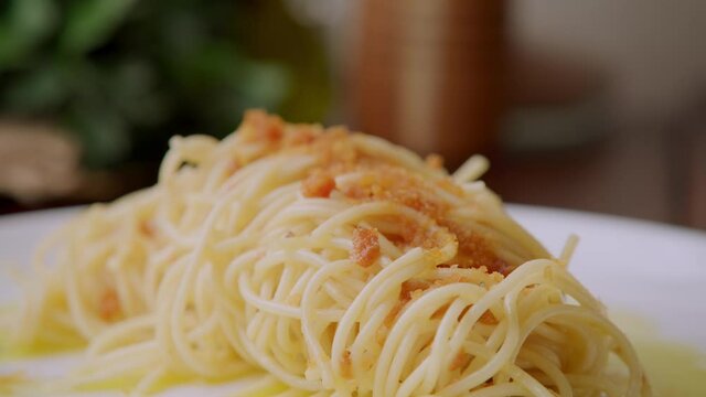 Garnishing delicious tasty traditional Italian cooked yellow pasta dish, Spaghetti alla bottarga, olive oil, cured mullet fish roe, detail close up slow motion