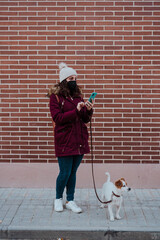 woman wearing protective mask, using mobile phone, walking at the city with her adorable jack russell dog. Lifestyle outdoors