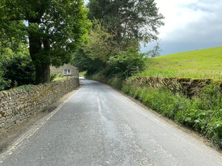 Looking along, the B6160 road, with dry stone walls, and a cottage near fields and trees in, Bolton Abbey, Skipton, UK
