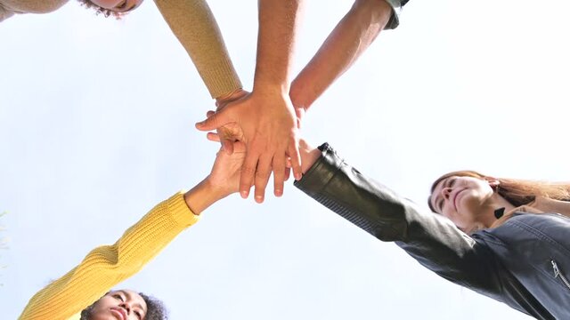 Friends and colleagues from different cultures and nationalities put their hands together against a bright sky and shake them as a symbol of unity
