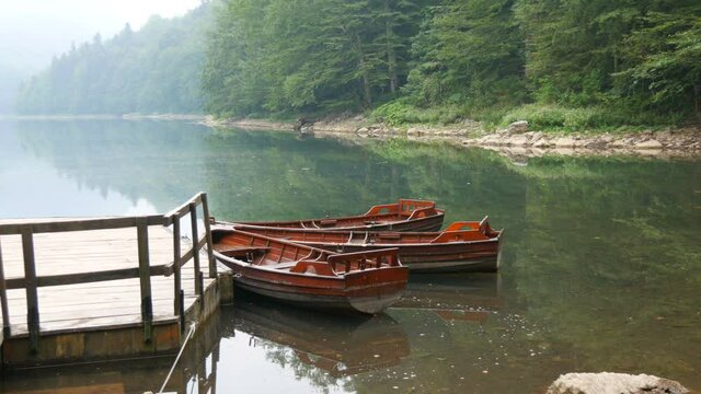 Wooden boats for walks on lake, empty without people near the shore on an incredibly beautiful lake with a misty morning haze. Mountain pond Biorgad Lake in Biogradska Gora National Park, Montenegro.