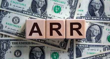 Wood cubes with acronym 'ARR' - 'annualized run rate' on a beautiful background from dollar bills. Business concept, copy space.