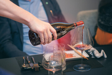 people pouring red wine to wineglass