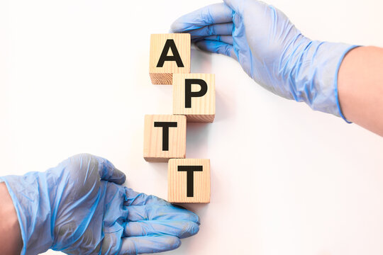 Word APTT on wooden cubes held by hands in protective gloves on a white background with available space for copying. the medicine
