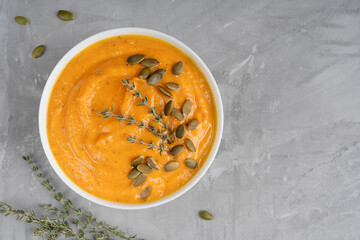 Vegetarian pumpkin soup made of pureed vegetables cooked on thanksgiving decorated with seeds and thyme served in bowl on gray concrete background. Image with copy space, horizontal orientation