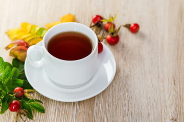 A Cup of tea on a napkin with fresh rosehip berries on a wooden surface 