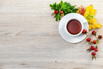 Tea with  fresh rosehip berries on a wooden surface with space for text.