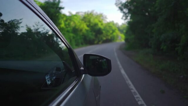 shot of the side of a moving car down a road in the woods