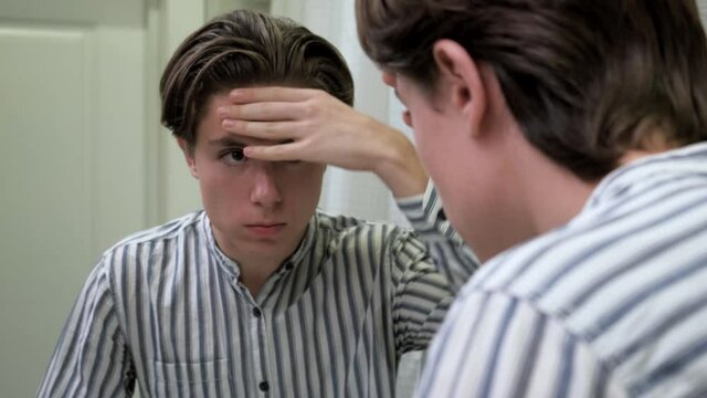 Young guy crushes pimples in the bathroom. Problems with the skin. Dermatology